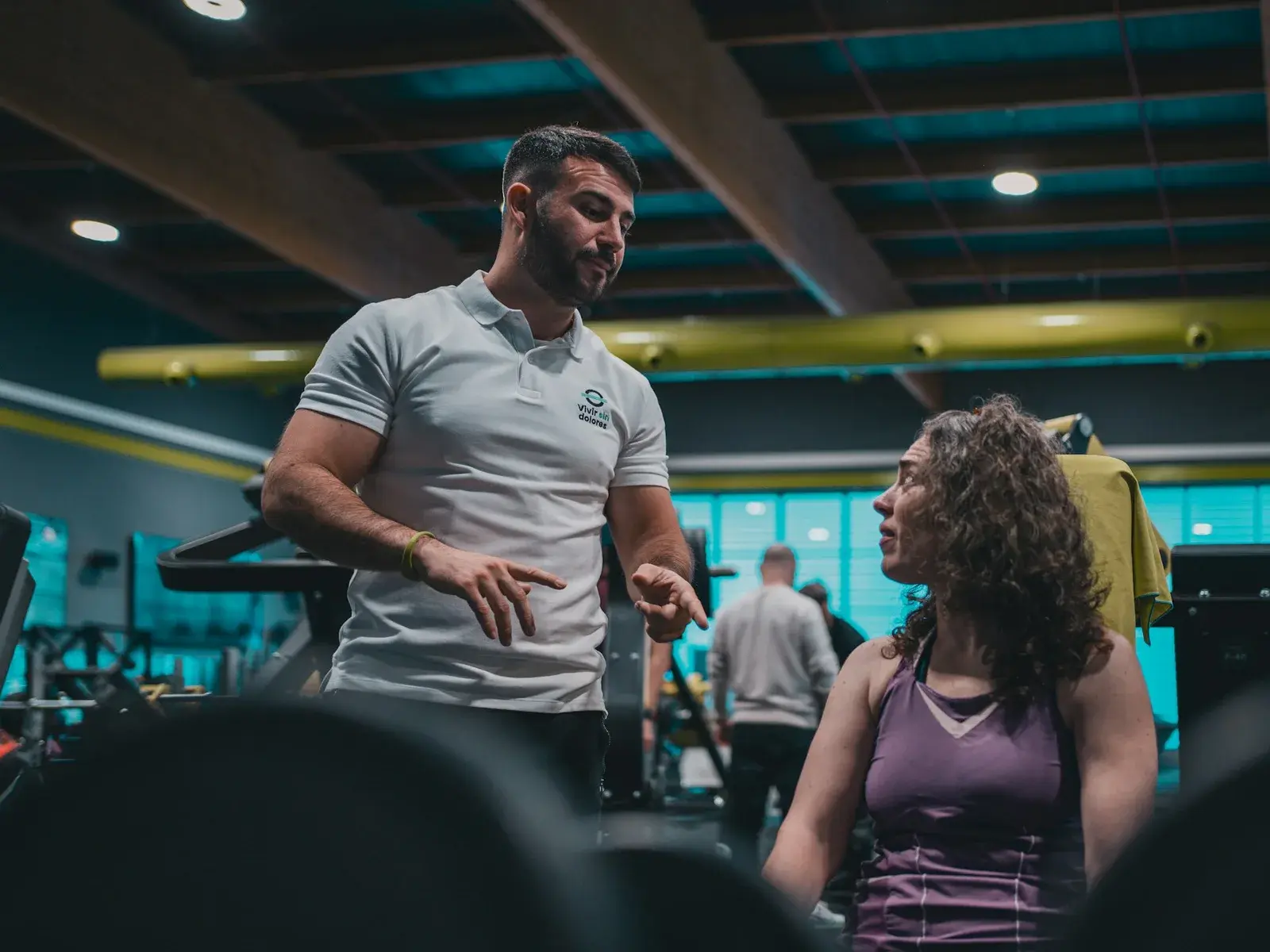 Entrenador personal hablando con un cliente junto al rack de una sala de pesas